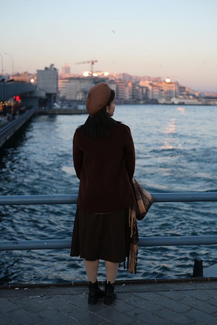 A woman with a beret admires the sea from Istanbul's waterfront at twilight.