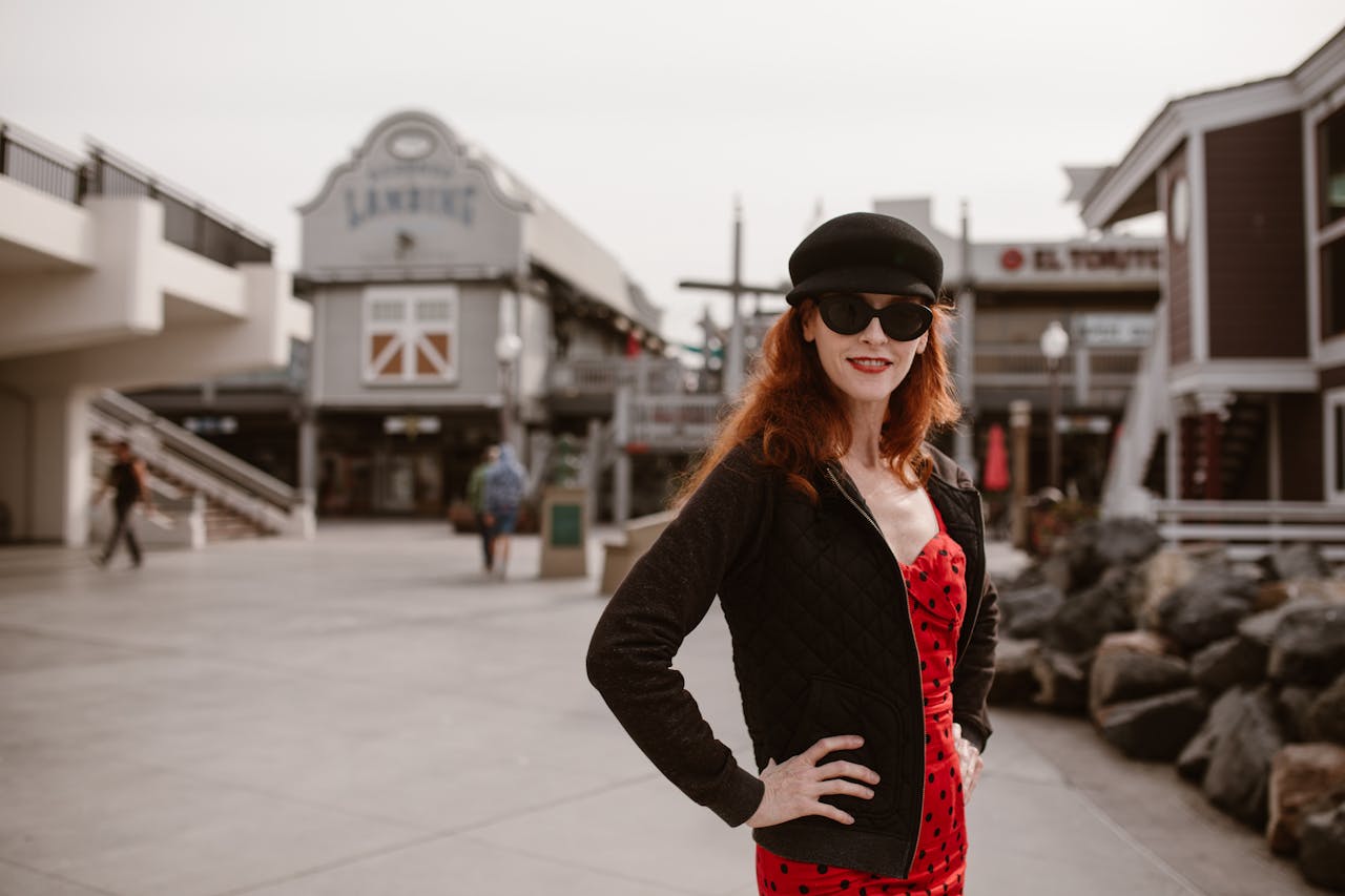 about-us A fashionable woman in sunglasses and a black hat poses confidently in a city street.